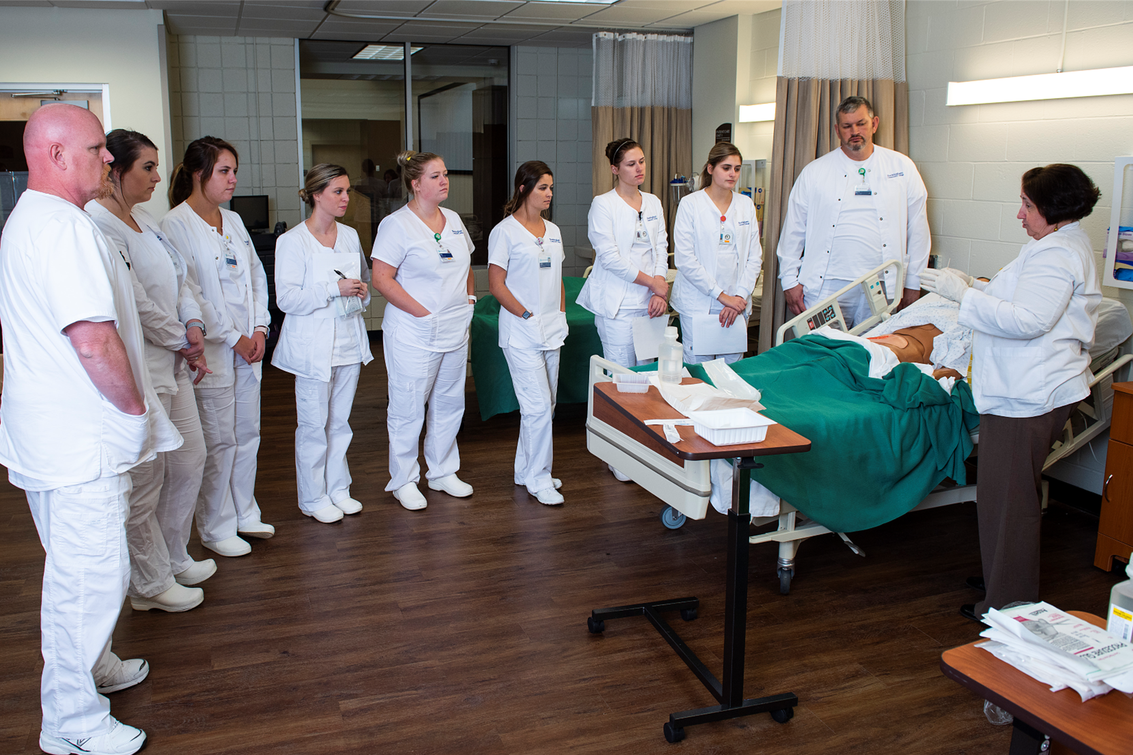 Group of medical students being taught by an instructor who is standing by a manikin.