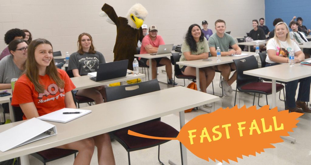Students smiling in a classroom with the RCC Eagle mascot waving.
