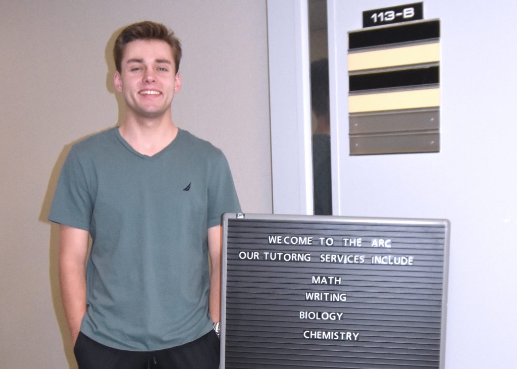 Student Colby Gunter stands by the sign to a tutoring center.